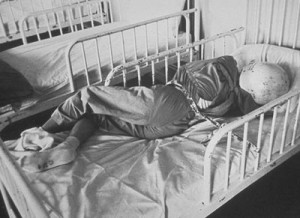 Child chained in bed wearing protective headgear and mask