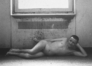 Unclothed male resident of an institution lies before a radiator, circa 1960s